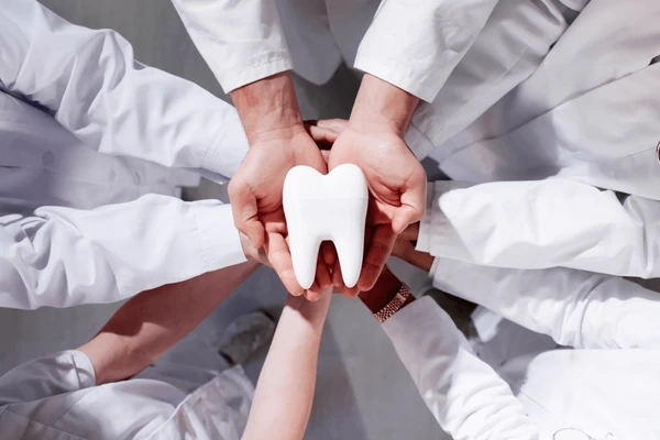 dental team members placing hands together around a white tooth model at honeycomb dental